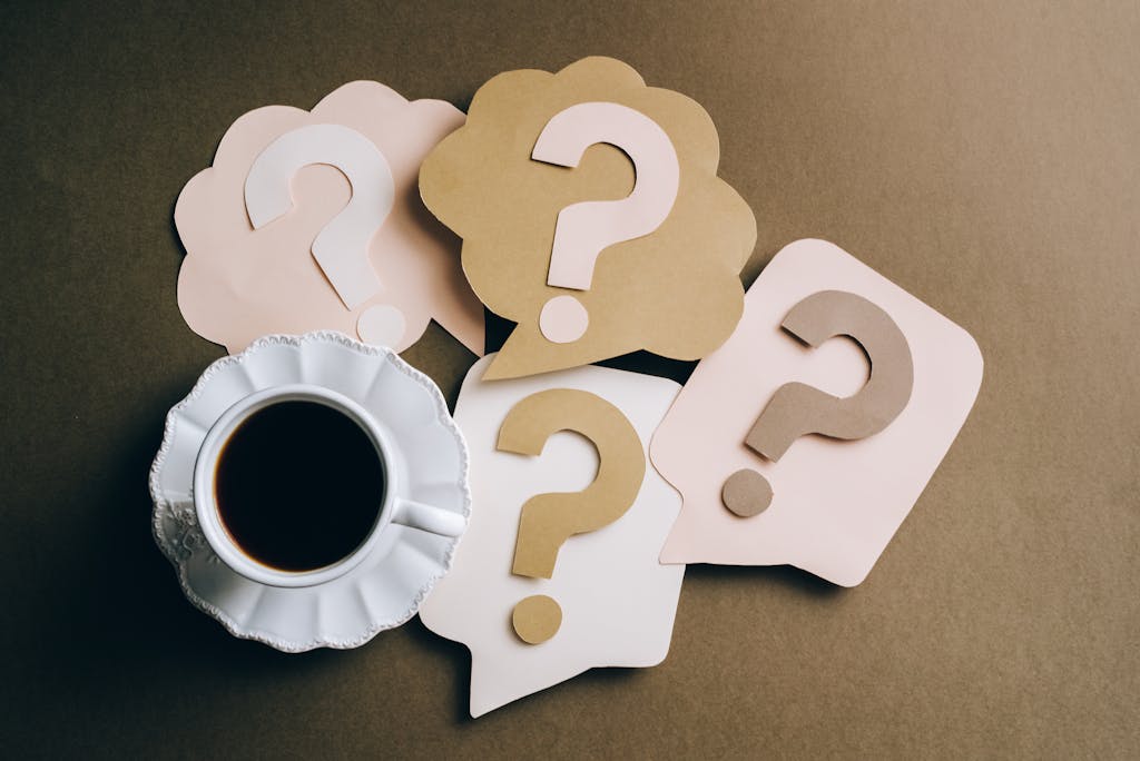 FAQs 1 Creative concept with coffee cup and paper question marks on a table. For FAQs page
