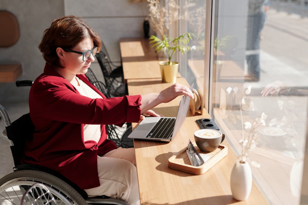 Accessibility 1 Woman in wheelchair working on a laptop in a bright café, showcasing a remote work lifestyle. for accessibility page